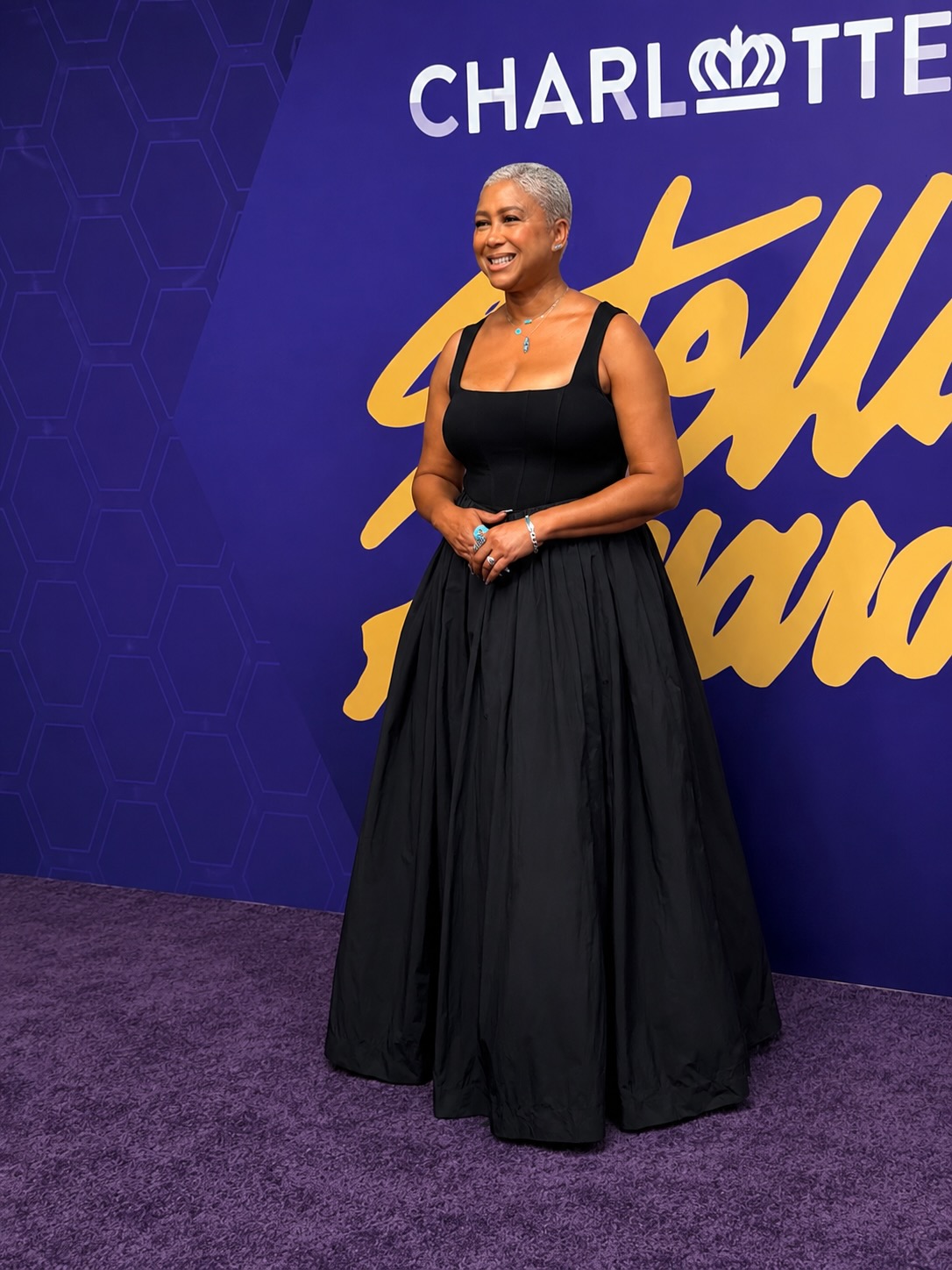 A woman in a black dress standing in front of a large "Charlotte" logo on a purple background.