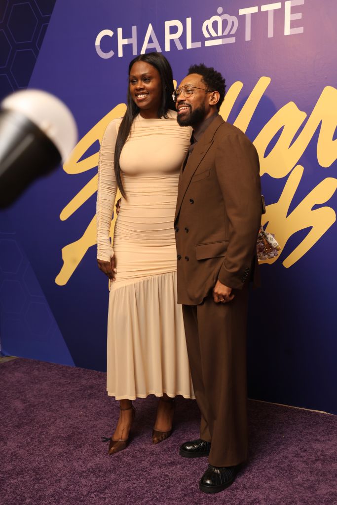 A smiling couple posing in front of a large "Charlotte" sign at an event or premiere.