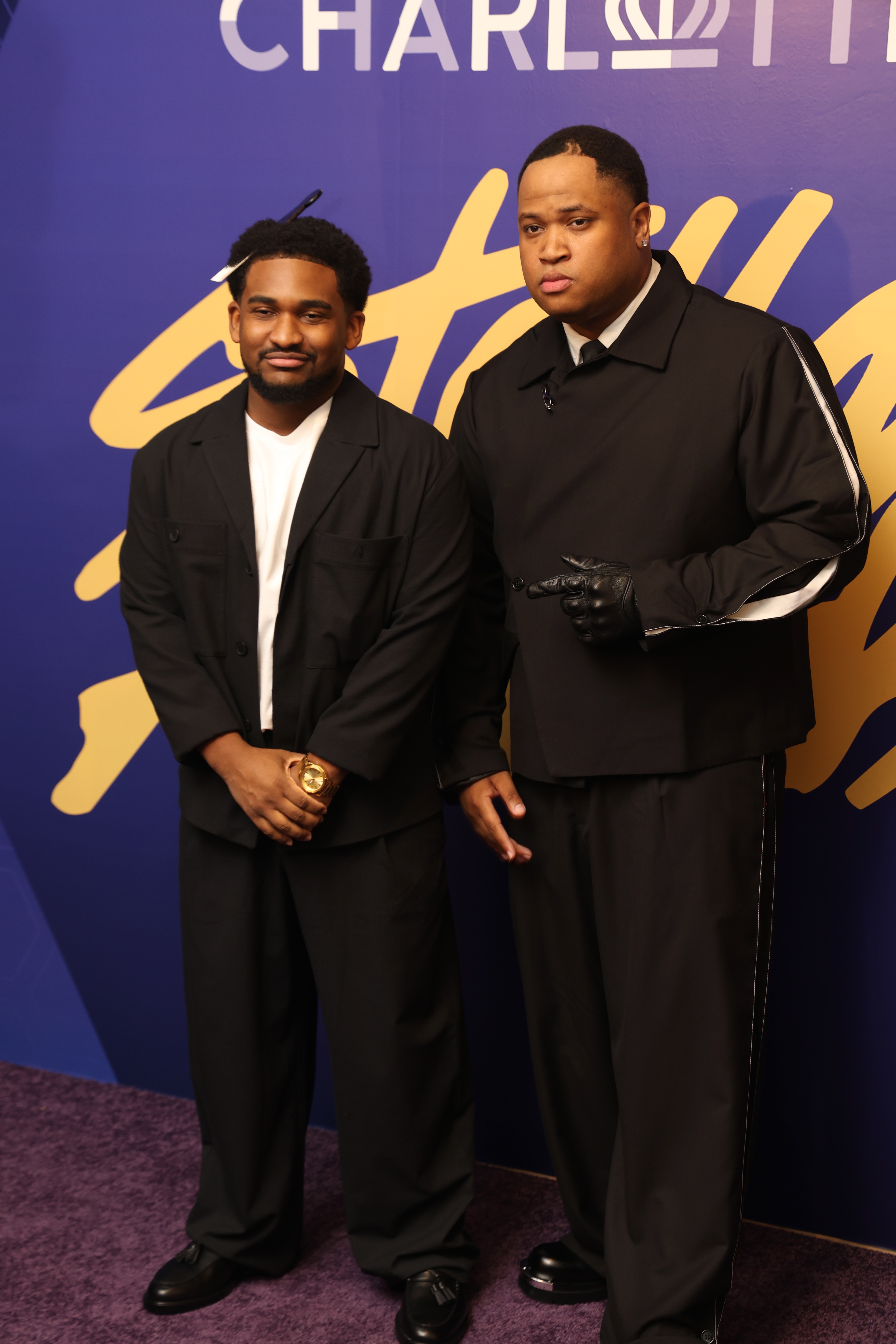 Two men in black suits standing in front of a purple background with the "Charli" logo.