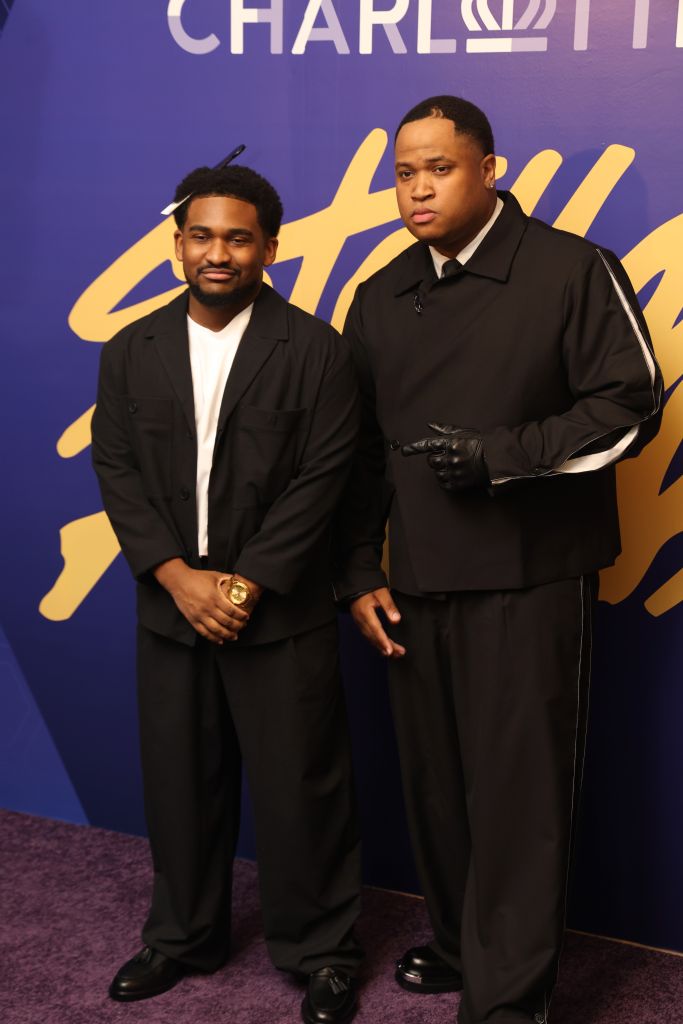 Two men in black suits standing in front of a purple background with the "Charli" logo.