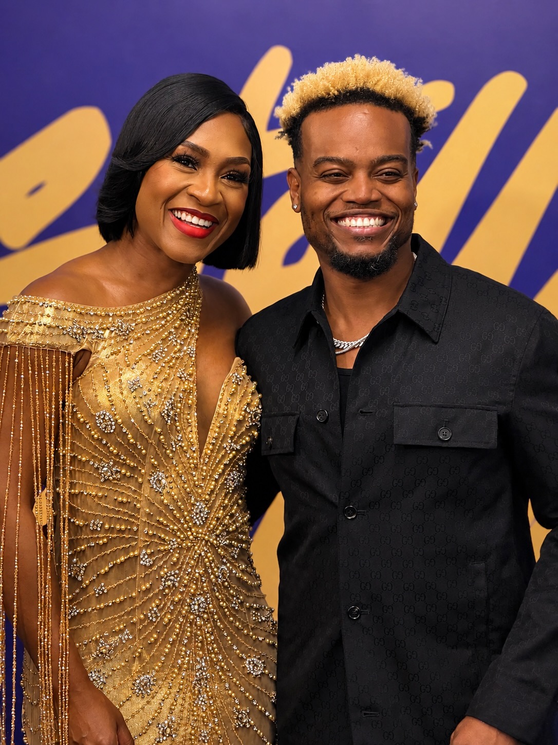Two smiling people posing together, a woman in a sparkling gold dress and a man in a black jacket.