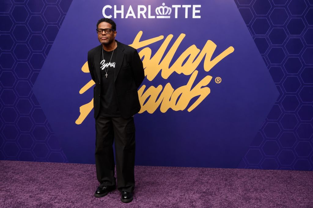 A man wearing a black shirt and pants stands in front of a purple background with the "Charlotte Hornets" logo and the text "Swarm Mob" displayed.